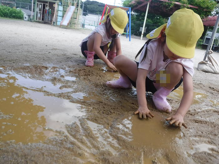 雨上がりの園庭の泥で遊ぶ5歳児