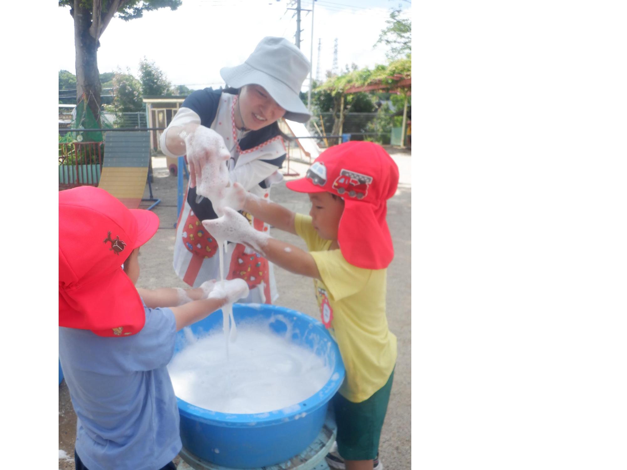 子どもと先生がたらいの中の泡に触れて遊んでいる様子
