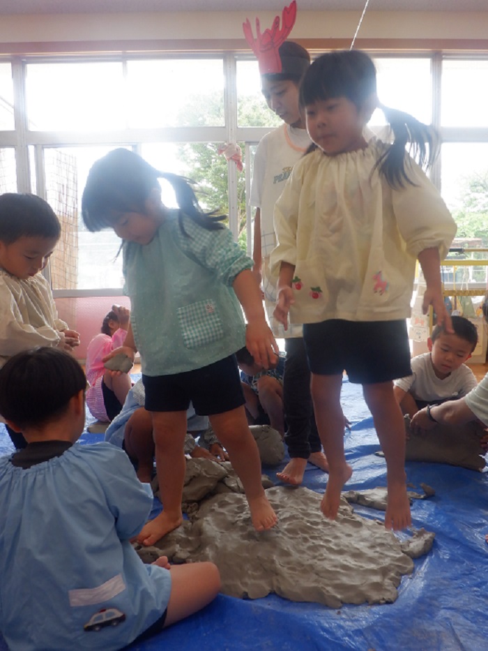 裸足になって土粘土を踏んだり、手で触ったりしている4歳児