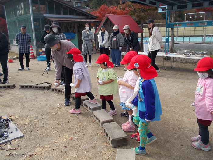 さつまいもを焚火に入れる子ども達