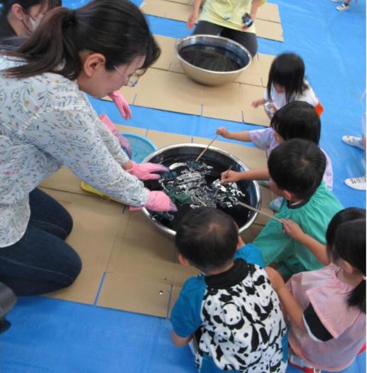 智浄先生と一緒に藍染め液にハンカチをつける3歳児