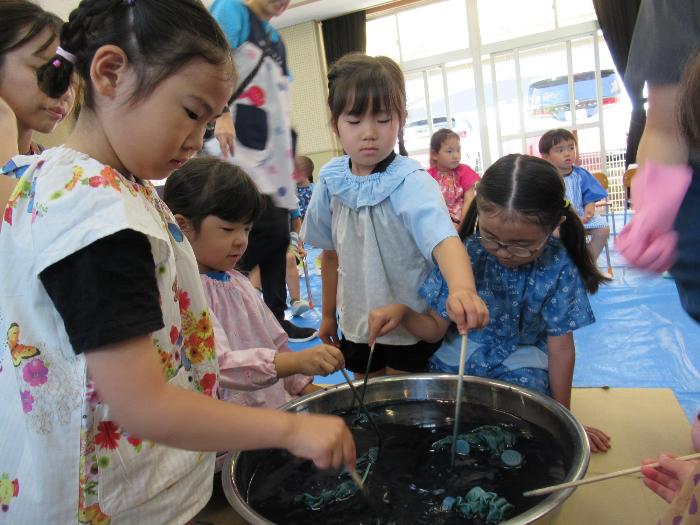 自分で絞ったTシャツを藍染め液につける5歳児