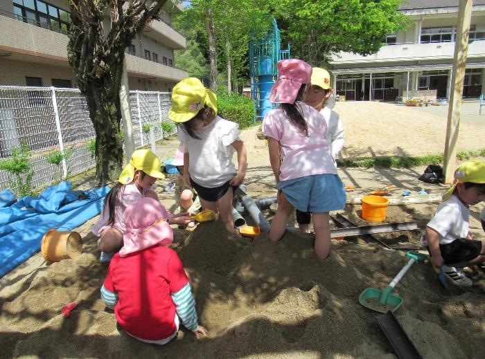 砂場遊びで足を埋めて楽しんでいる4・5歳児