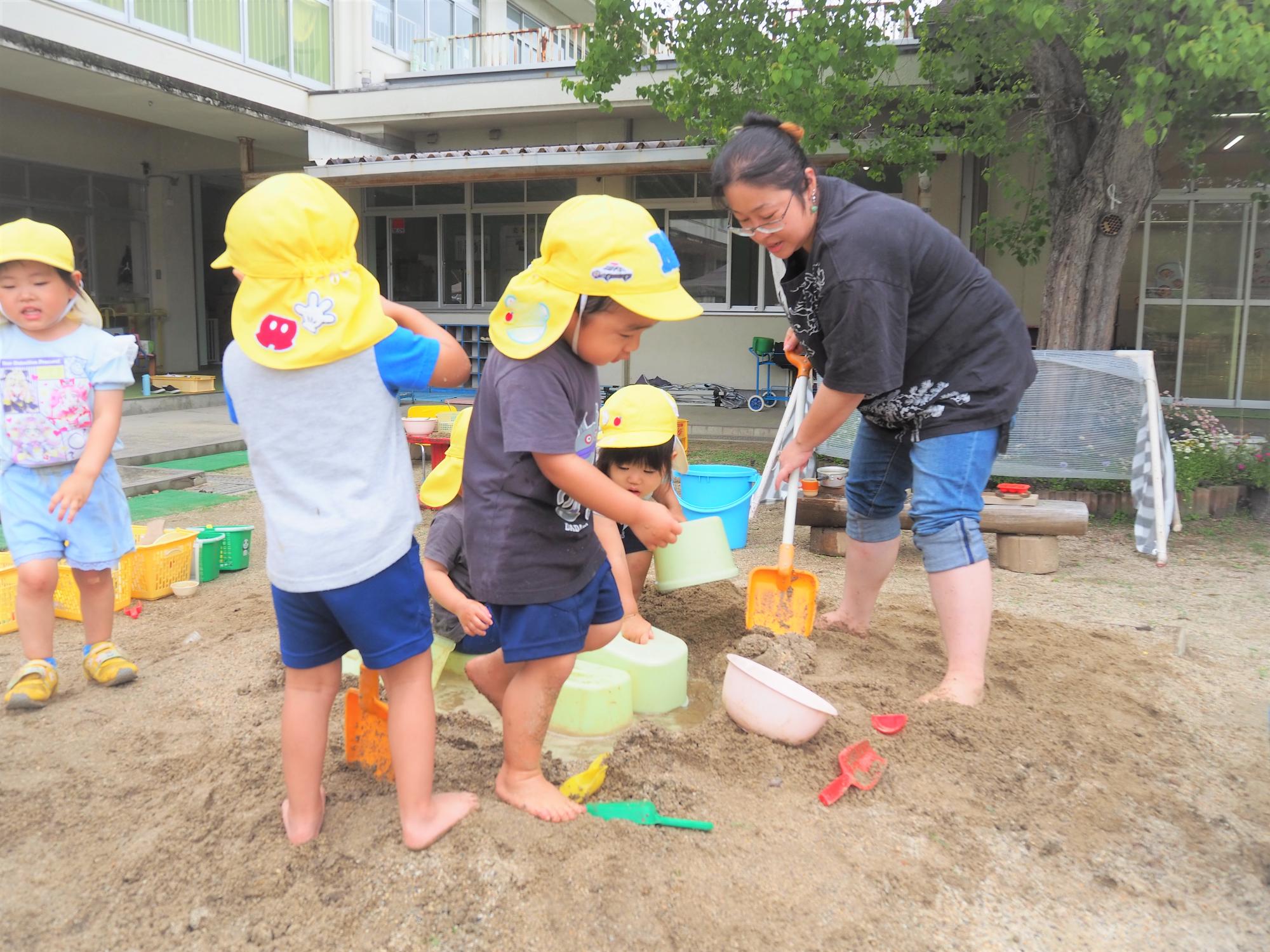 保護者と一緒に砂場で遊んでいる子どもたち