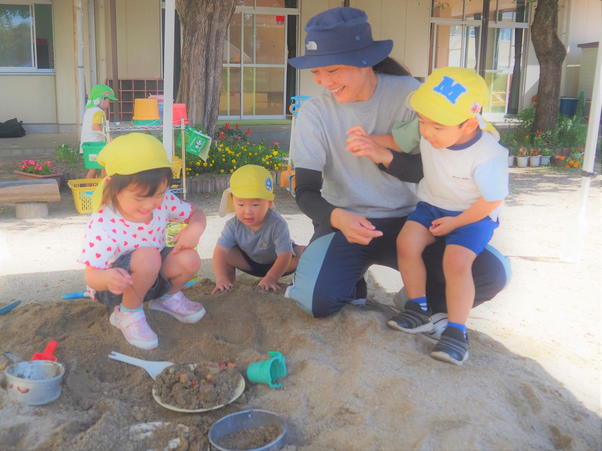 砂場でケーキを作り担任の誕生日を祝う3歳児