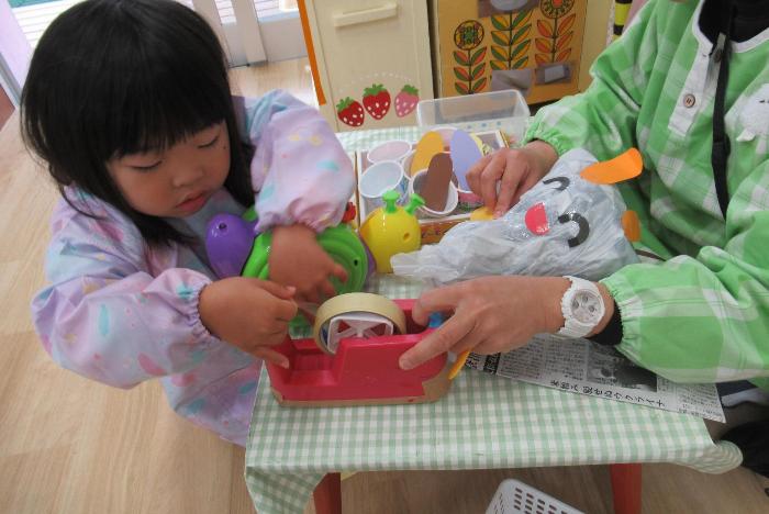 ビニールぶくろをテープでくっつけて人形を作っている3歳児