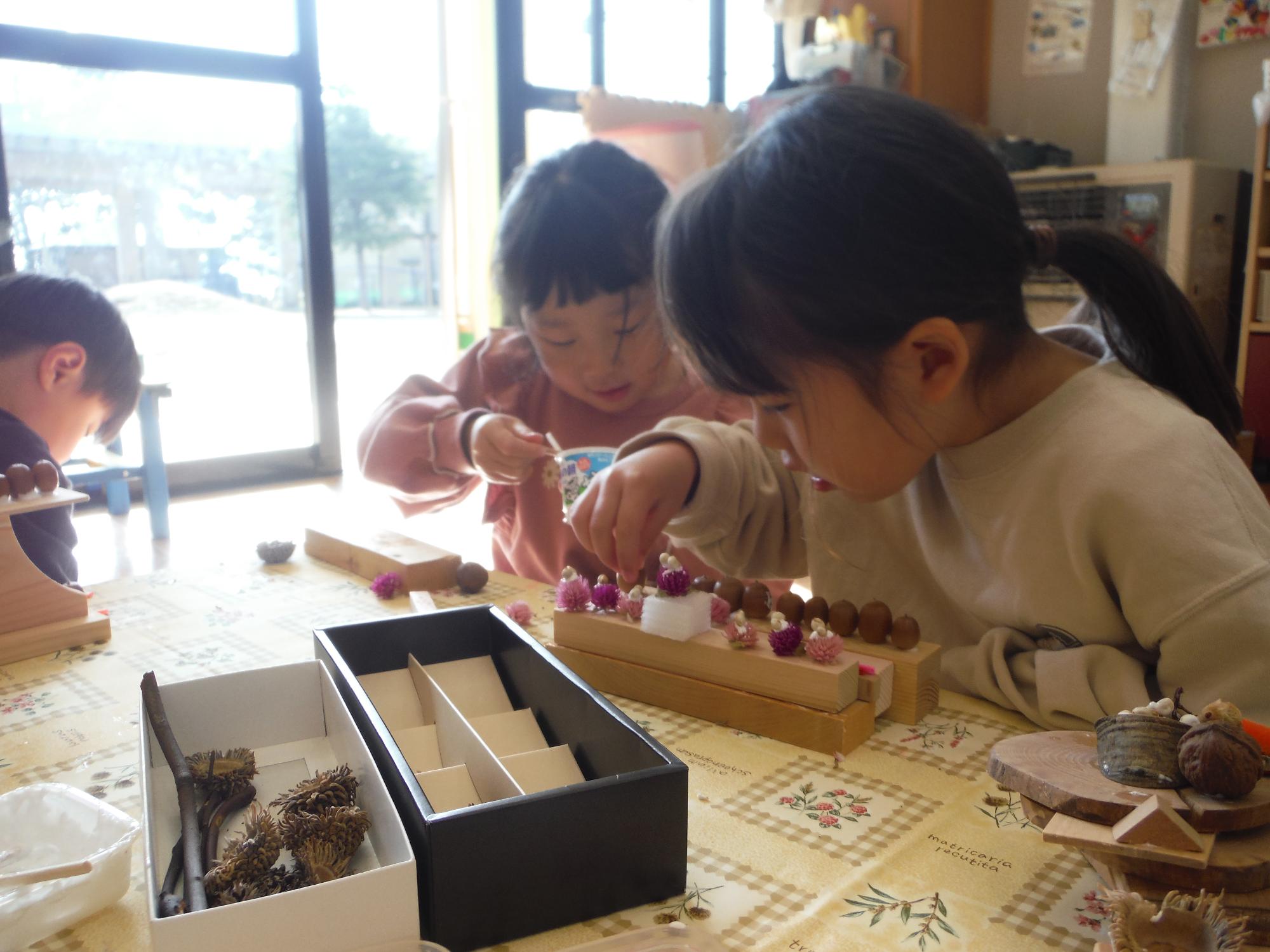 木の実や花を使ってケーキの飾りつけをしている子どもの様子