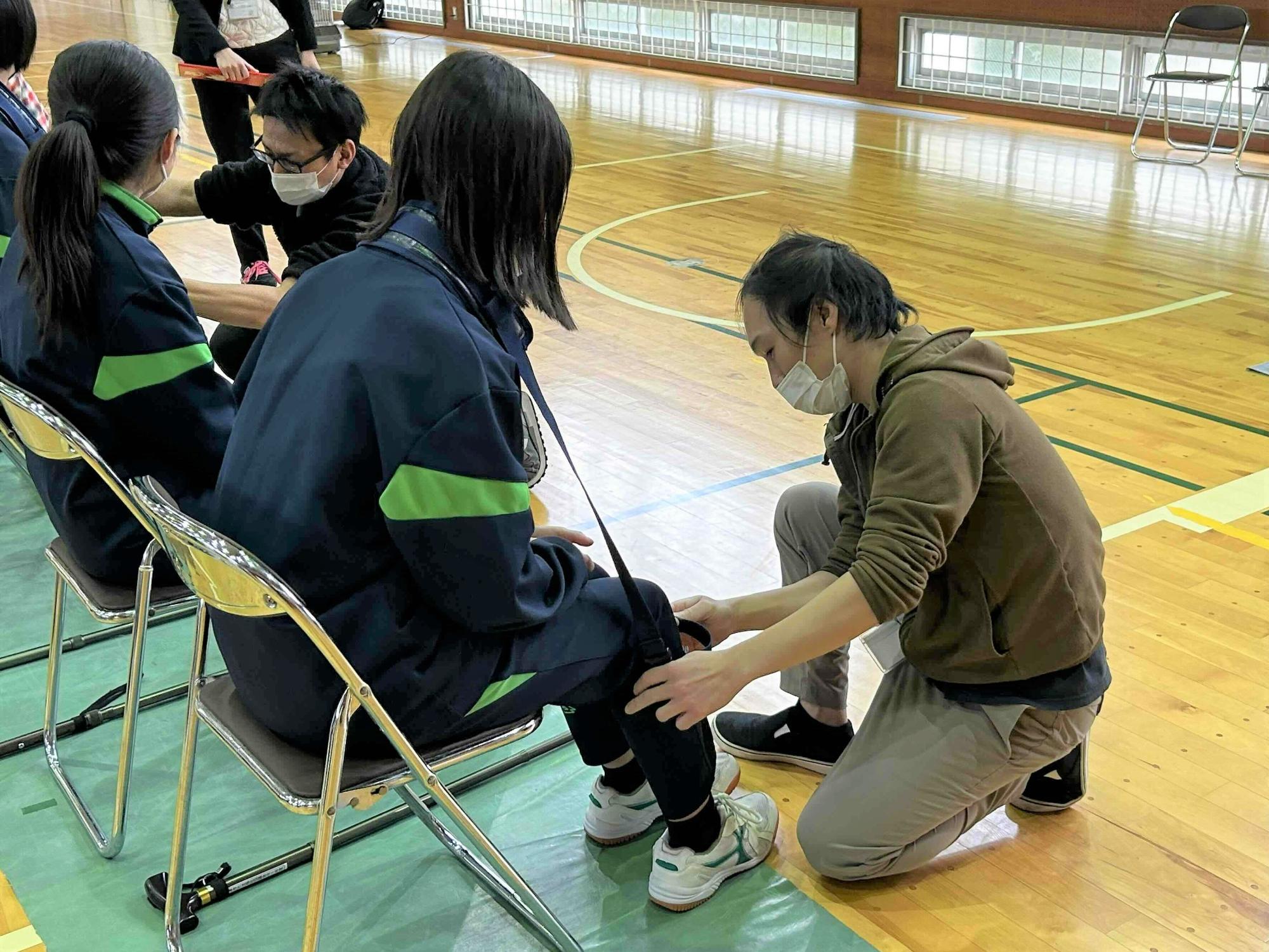 高齢者疑似体験グッズを生徒につけてあげている介護職員の様子