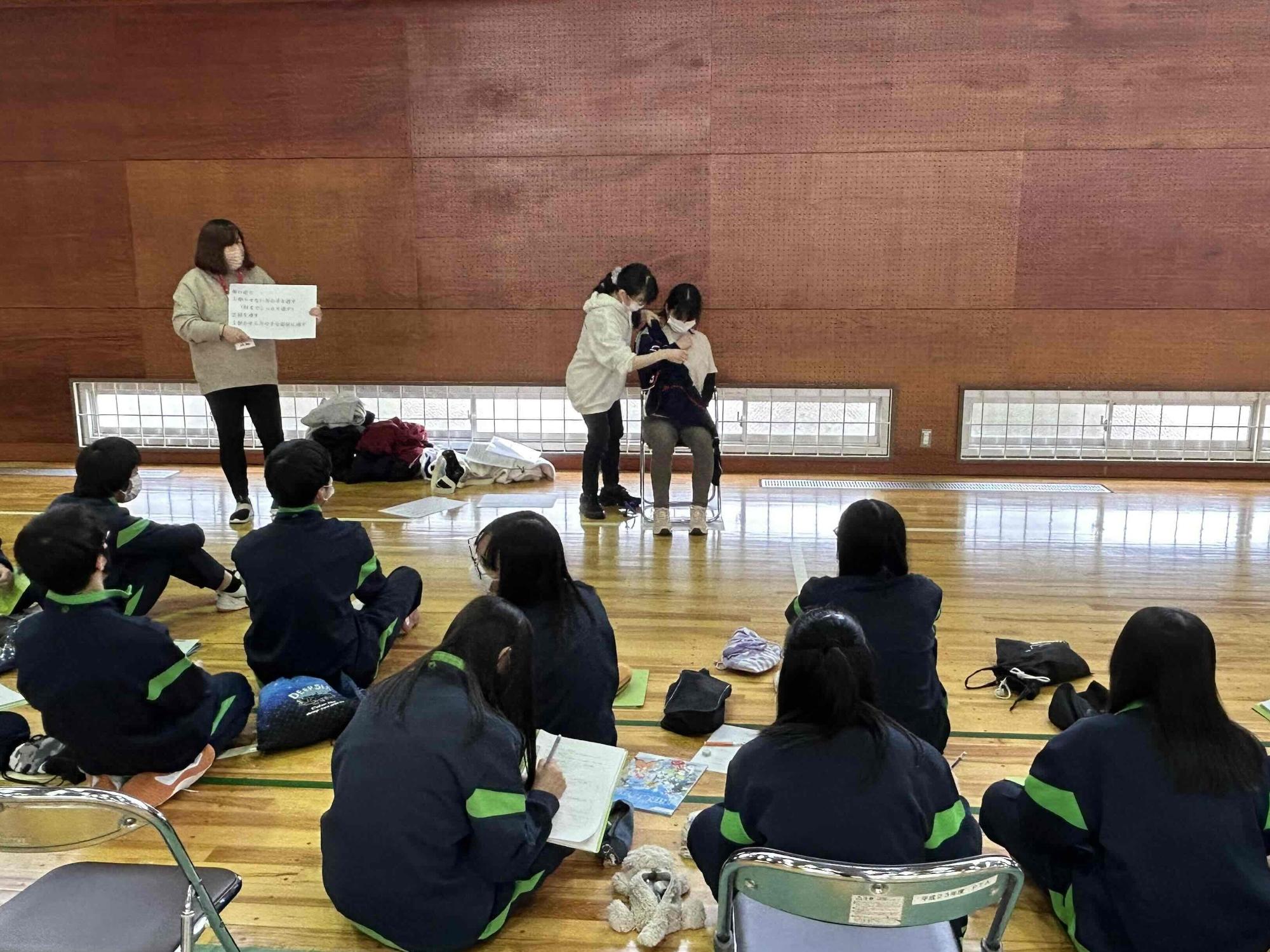 右腕がまひした高齢者役の介護職員の着脱を解除する介護職員の様子