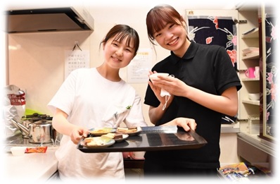 笑顔で料理の配膳をしている二人の女性の介護職員さんの写真