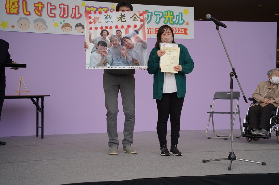 フォトコンテスト入賞に際し表彰を受け賞状を掲げる事業所職員の様子