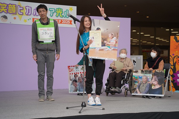 フォトコンテスト入賞に際し表彰を受け作品と賞状を掲げる事業所職員の様子