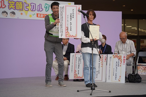 川柳コンテスト利用者部門入賞に際し表彰を受け賞状を掲げる事業所職員の様子